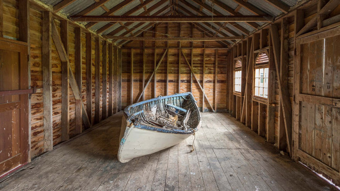 A white and blue row boat laying on an angle inside one of the farm buildings