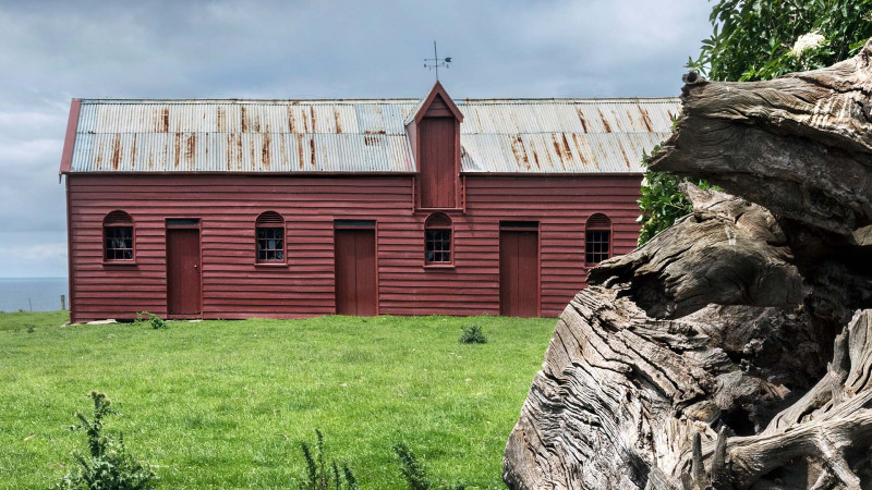 A reddish-brown pitsawn timber farm building in a paddock on a stormy day