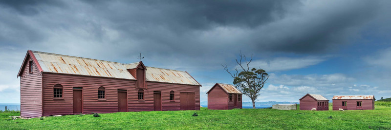 Matanaka reddish-brown pitsawn timber farm buildings across the paddock on a stormy day