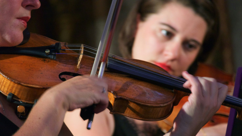 Close-up profiles of two women playing violins. 